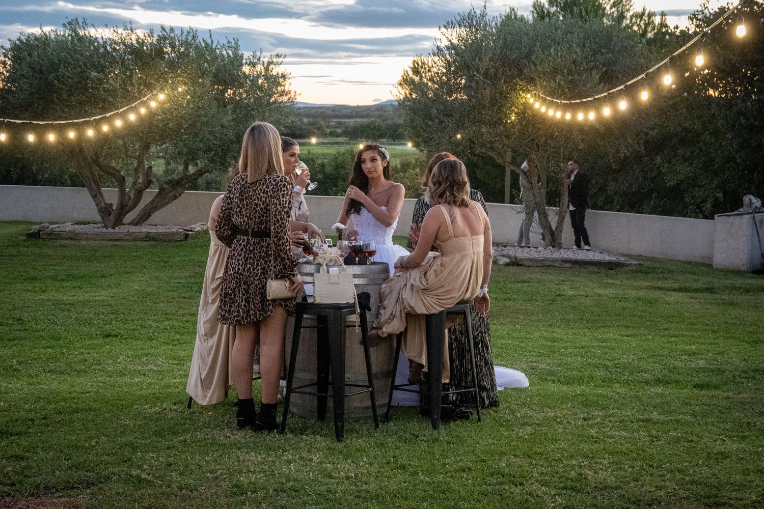 Outdoor reception setup with string lights and tables at sunset.