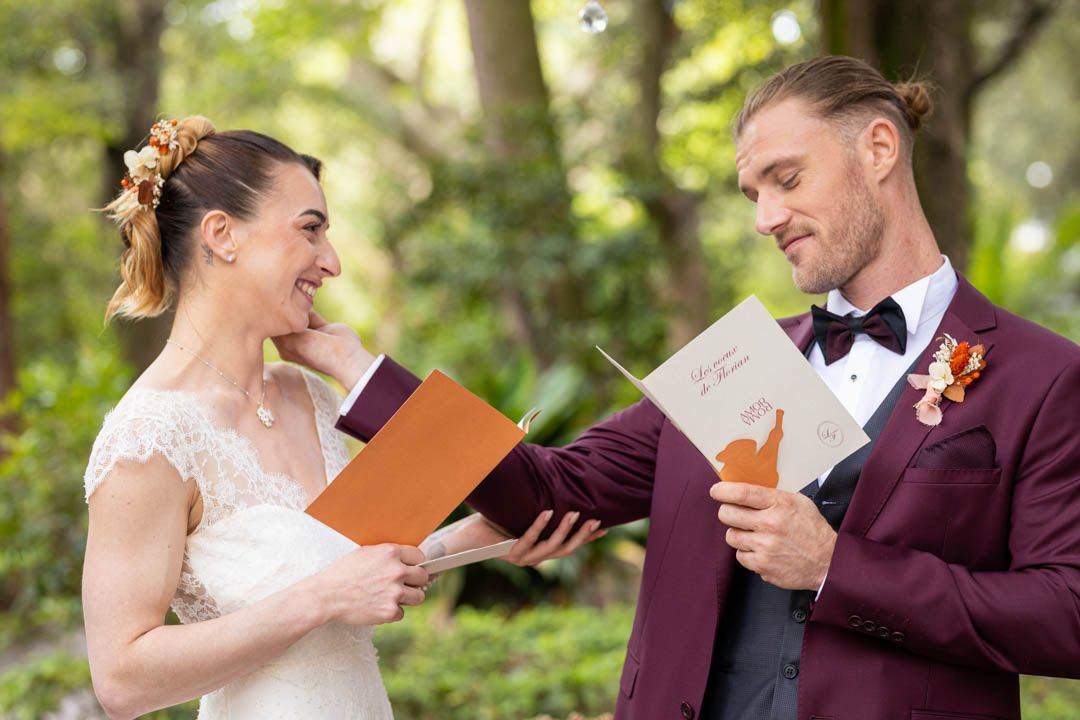 Couple in burgundy suit and lace dress share laughs while reading orange cards.