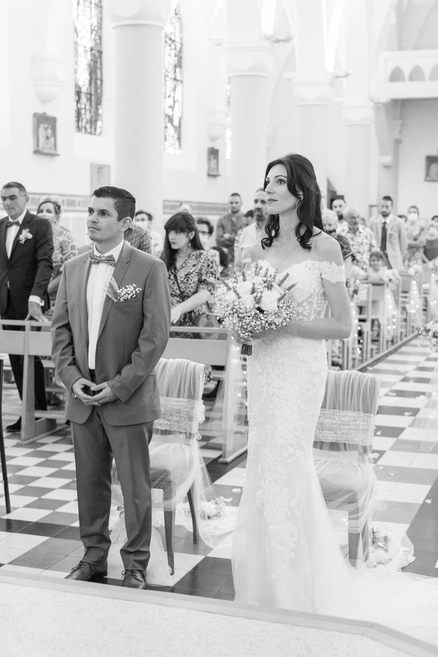 Wedding ceremony in a bright white church interior with black and white checkered floor.