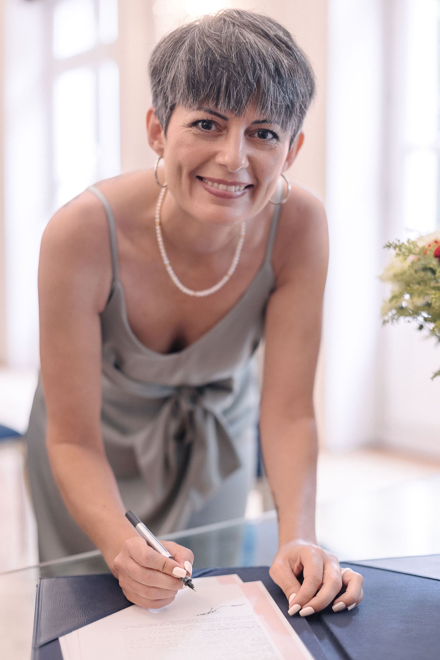 Wedding party member in silver dress signs official documents with a smile.