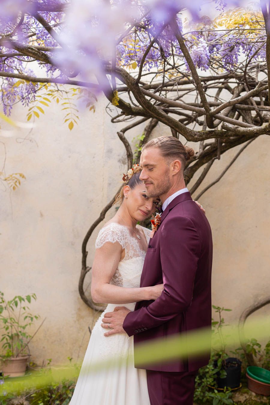 Romantic moment under blooming purple wisteria at an outdoor wedding venue.
