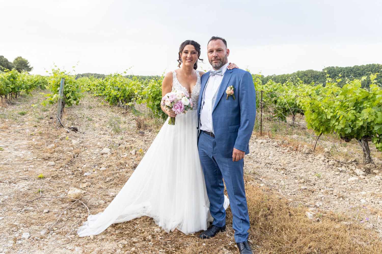 Bride and groom pose in vineyard setting with mountains in background.