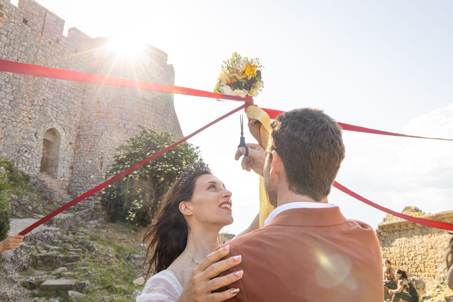 A romantic outdoor photoshoot in a sunlit garden venue with red fabric decor.