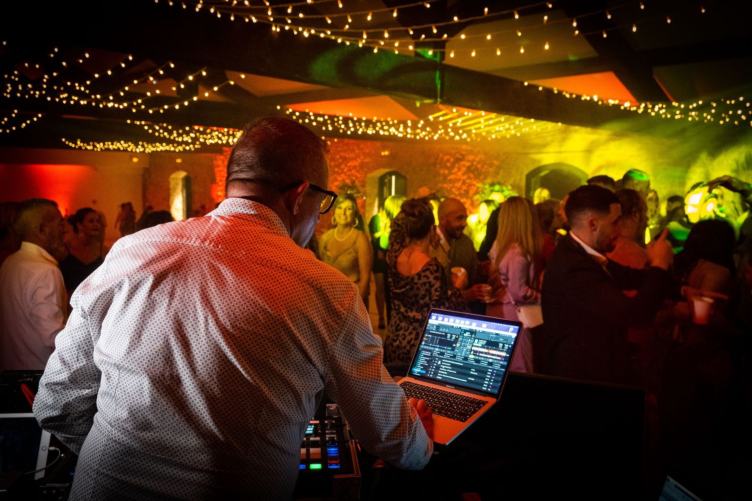 Wedding party celebration with colorful mood lighting and string lights overhead.