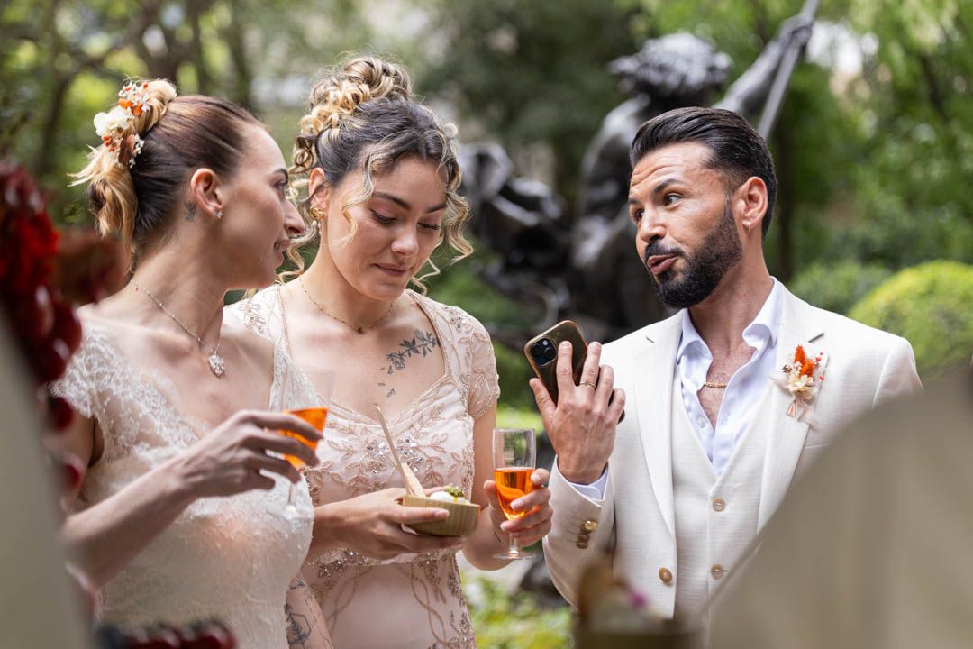 Wedding party guests enjoying cocktails and conversation in an outdoor garden setting with floral decorations.