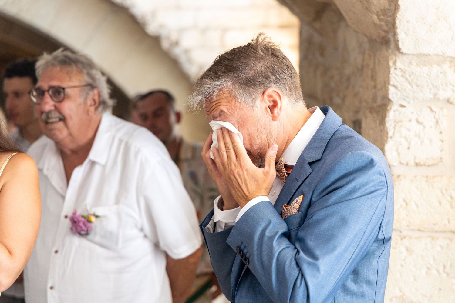 Wedding guest shows emotional reaction during ceremony in stone venue.