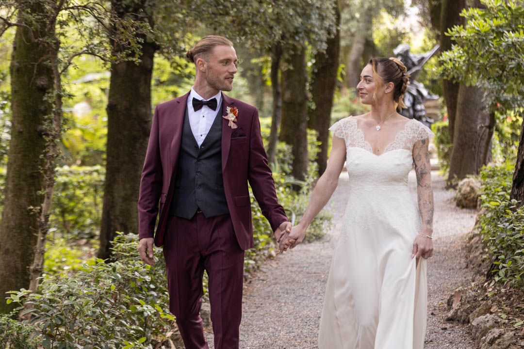 A wedding couple walks along a tree-lined path while sharing a joyful moment together.