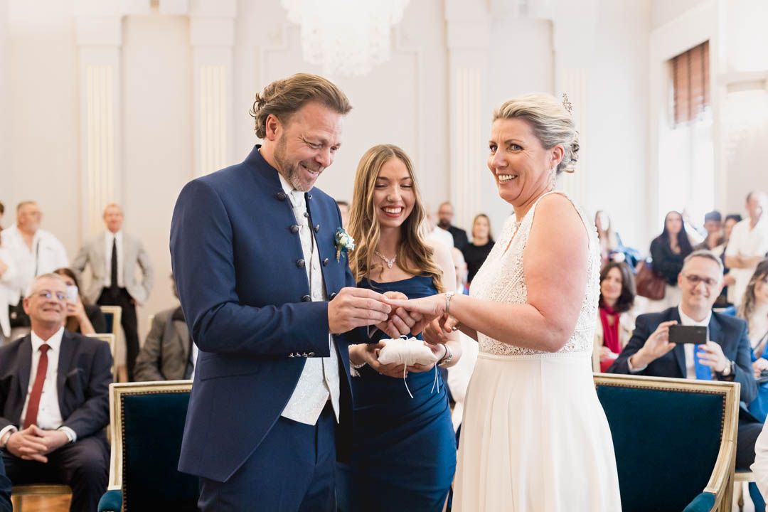 Wedding guests applaud and celebrate during an elegant indoor ceremony with white columns and decor.
