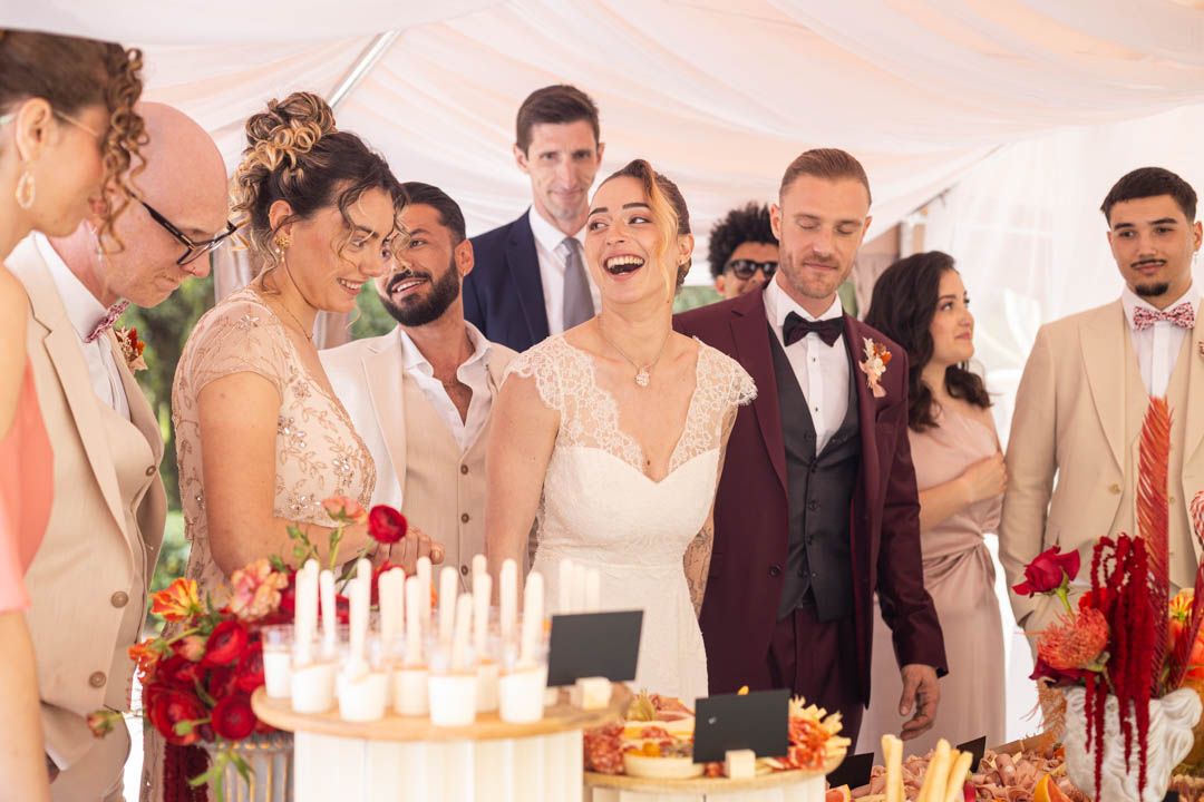 Wedding party gathered around a cake with candles celebrating at an elegant indoor reception.