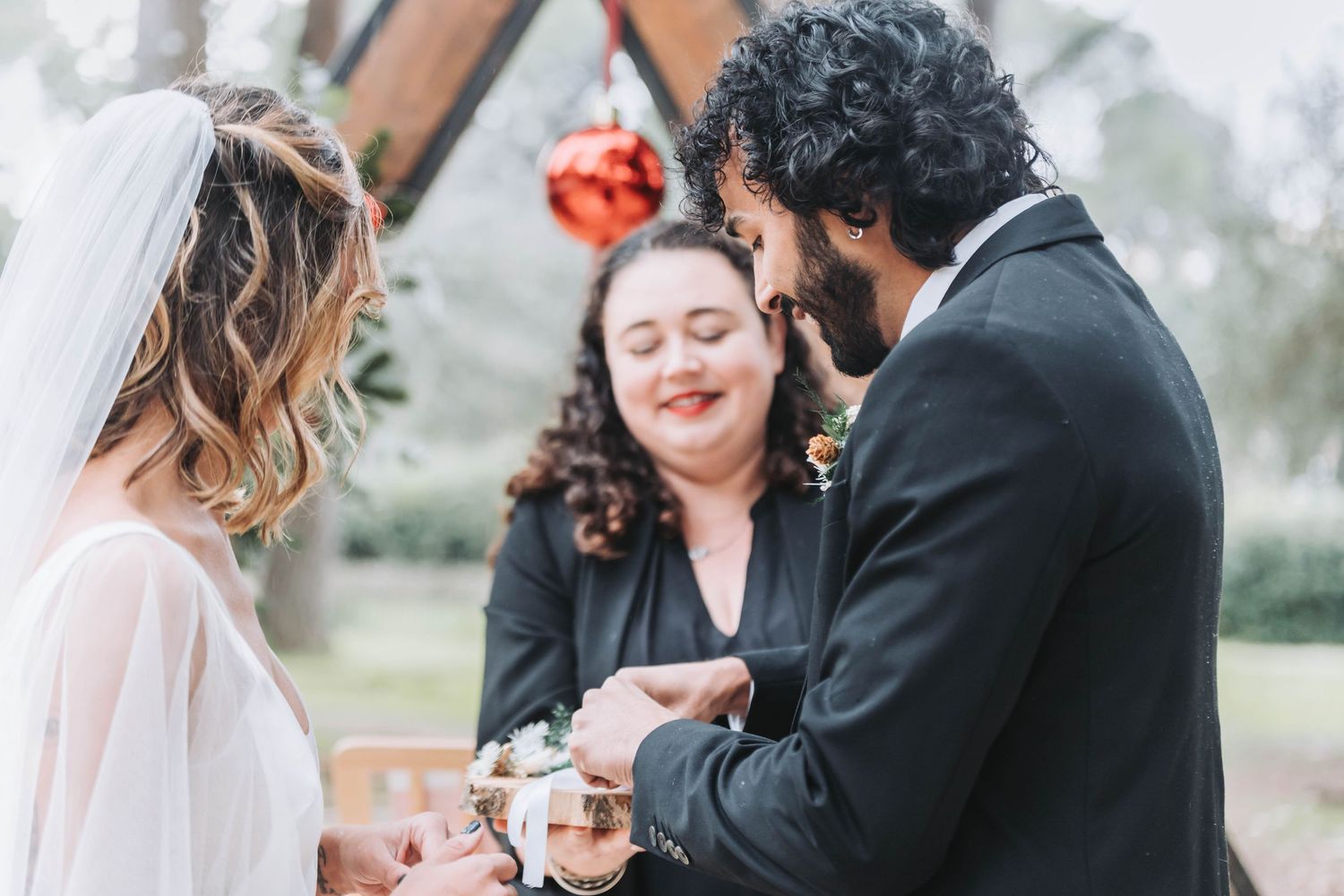Couple exchanges rings during outdoor winter wedding ceremony with wooden arch.