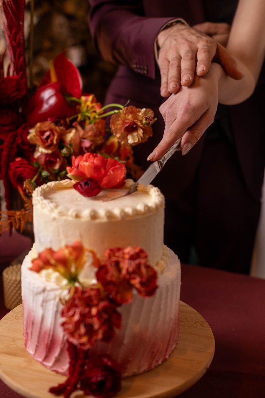 White wedding cake decorated with coral flowers on wooden table at reception.
