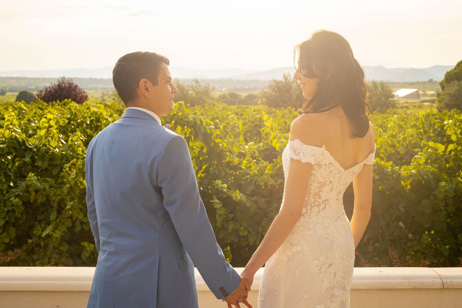 Backlit couple holding hands in vineyard during golden hour.
