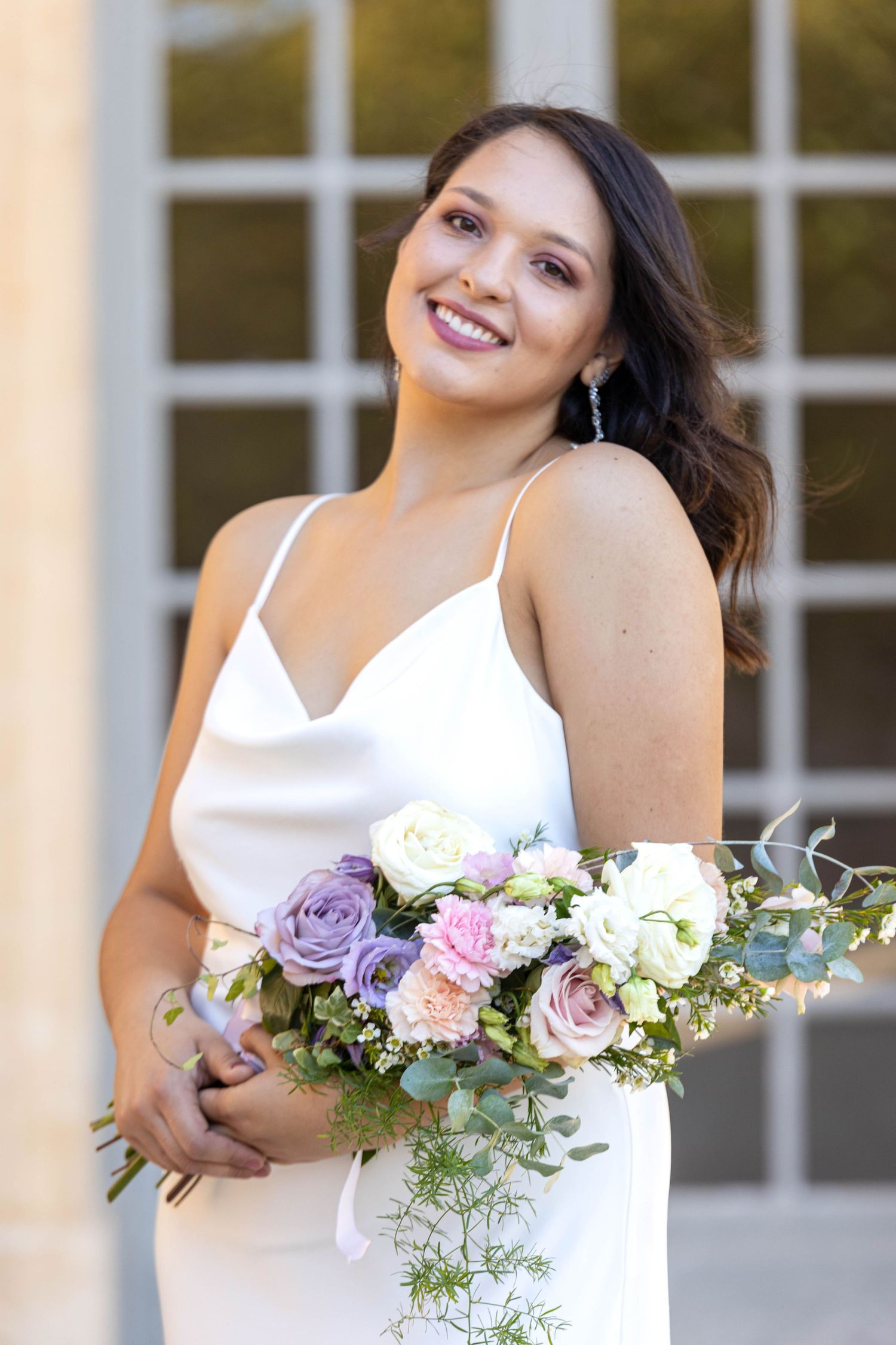 Bride in white dress holding romantic bouquet with purple and pink roses.