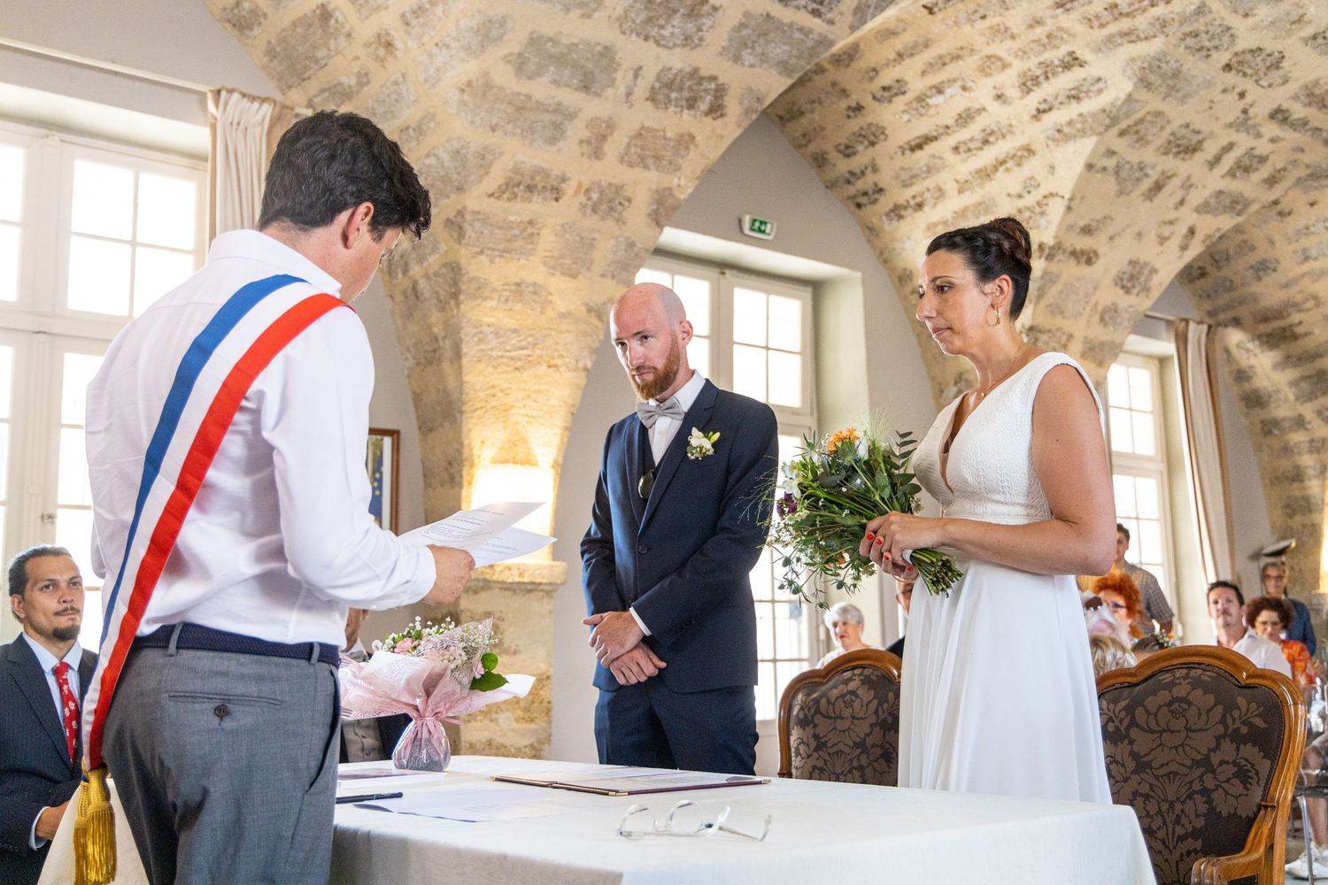 Civil ceremony takes place in historic stone room with official in tricolor sash.