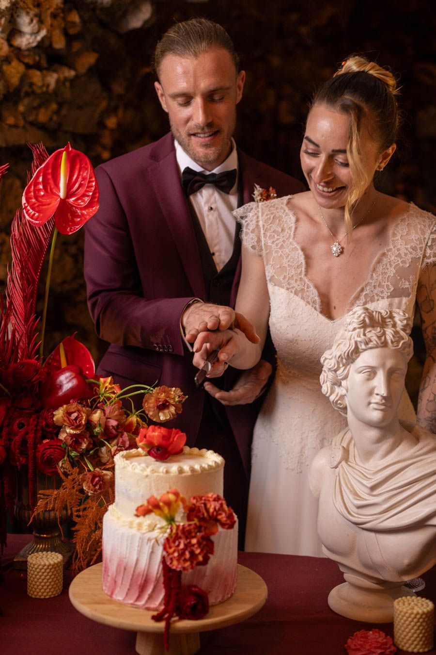 Wedding cake cutting scene with classical bust decoration and burgundy floral accents.