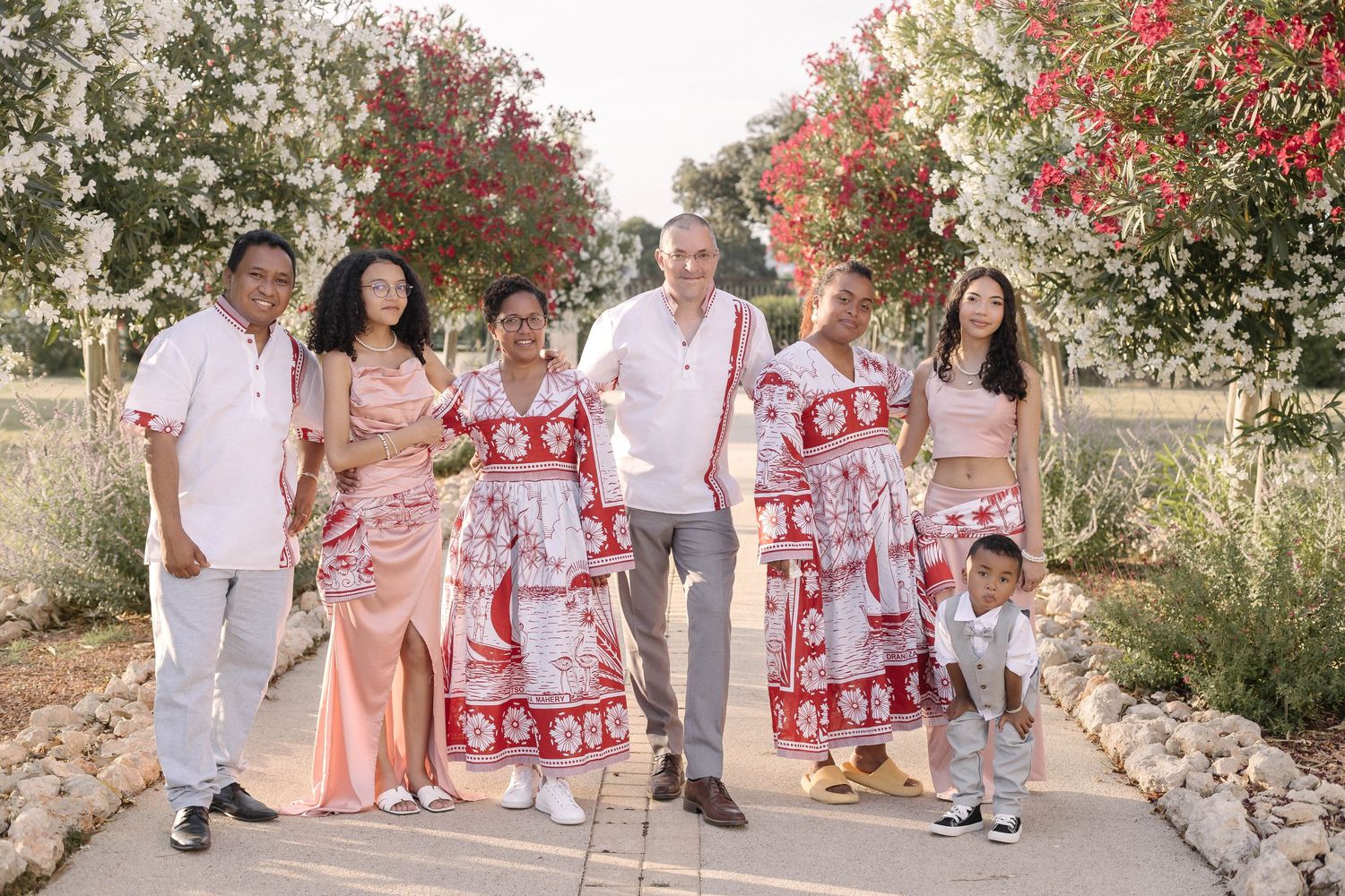 Wedding party in pink and floral outfits posing against stone wall backdrop.