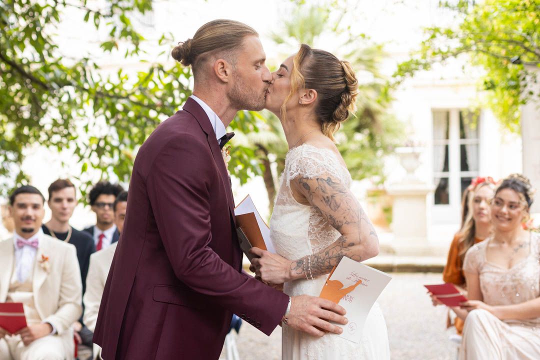 Wedding couple shares kiss during ceremony while guests look on.