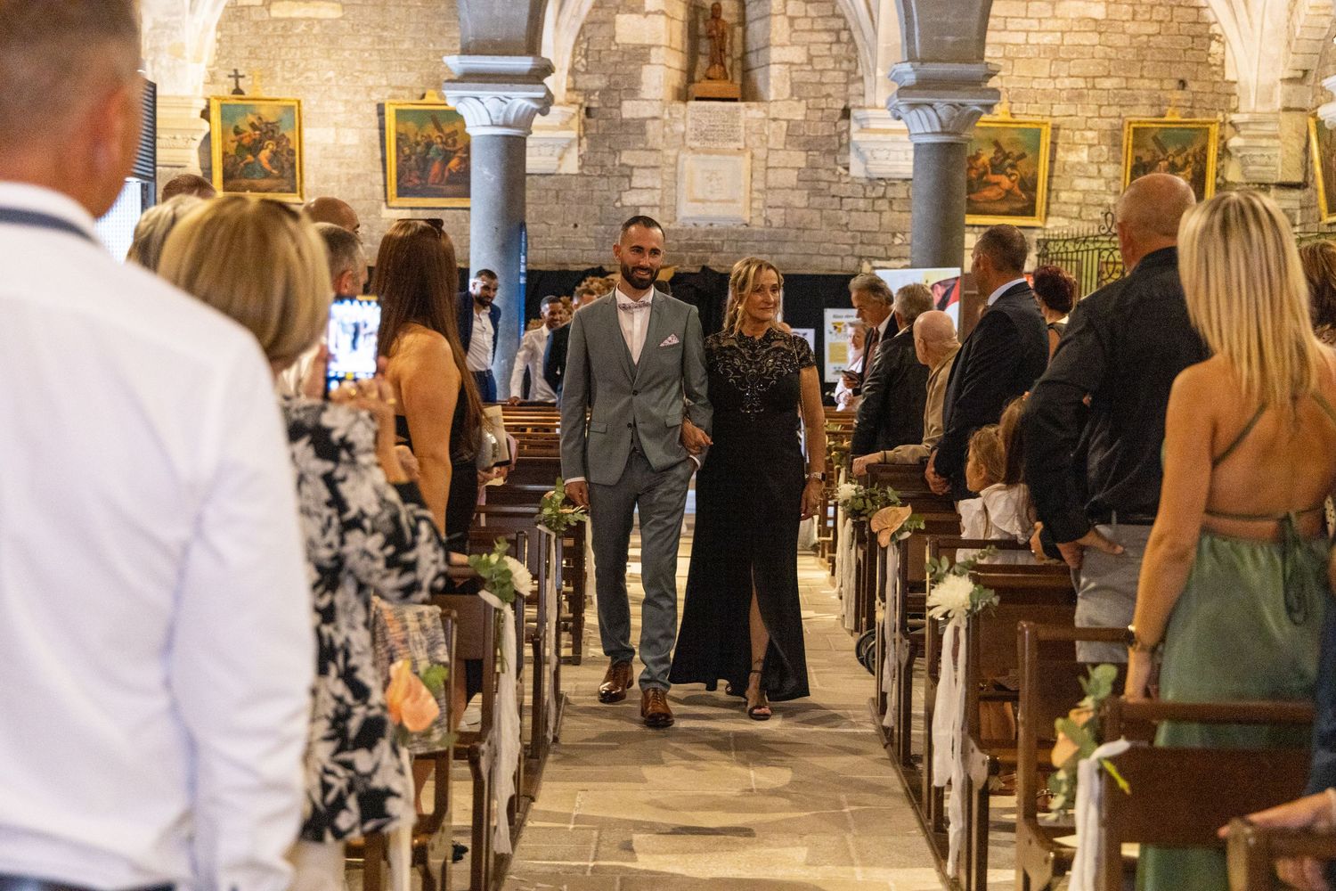Wedding guests gather in a historic stone church with arched ceilings for a ceremony.