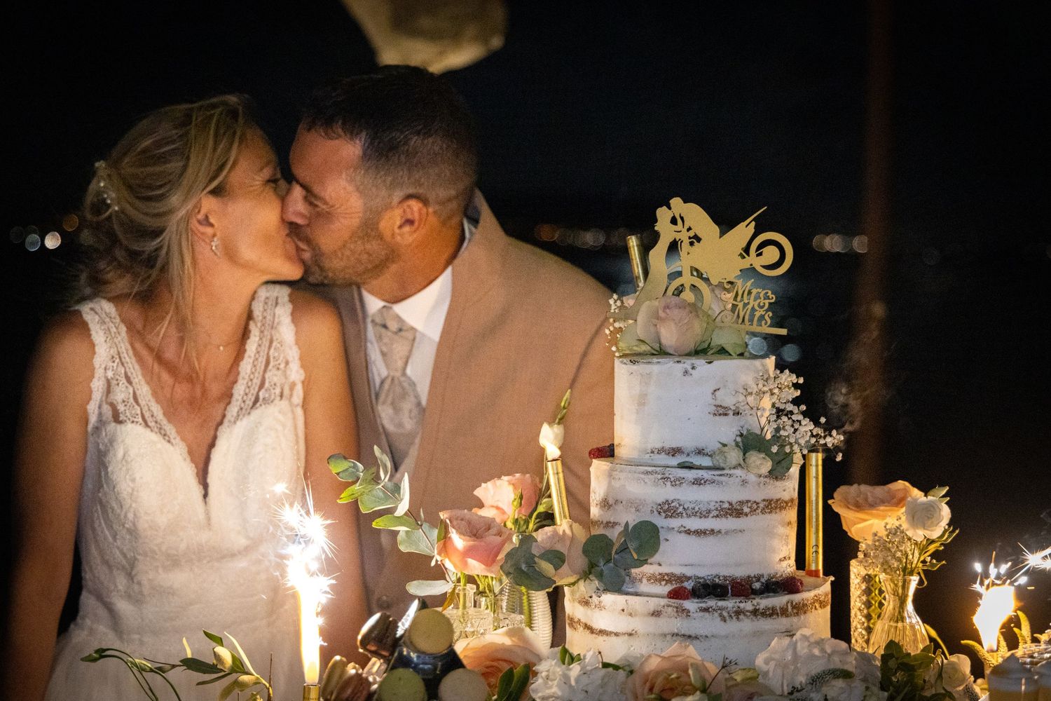 Romantic wedding cake moment with sparklers and elegant white tiered design.