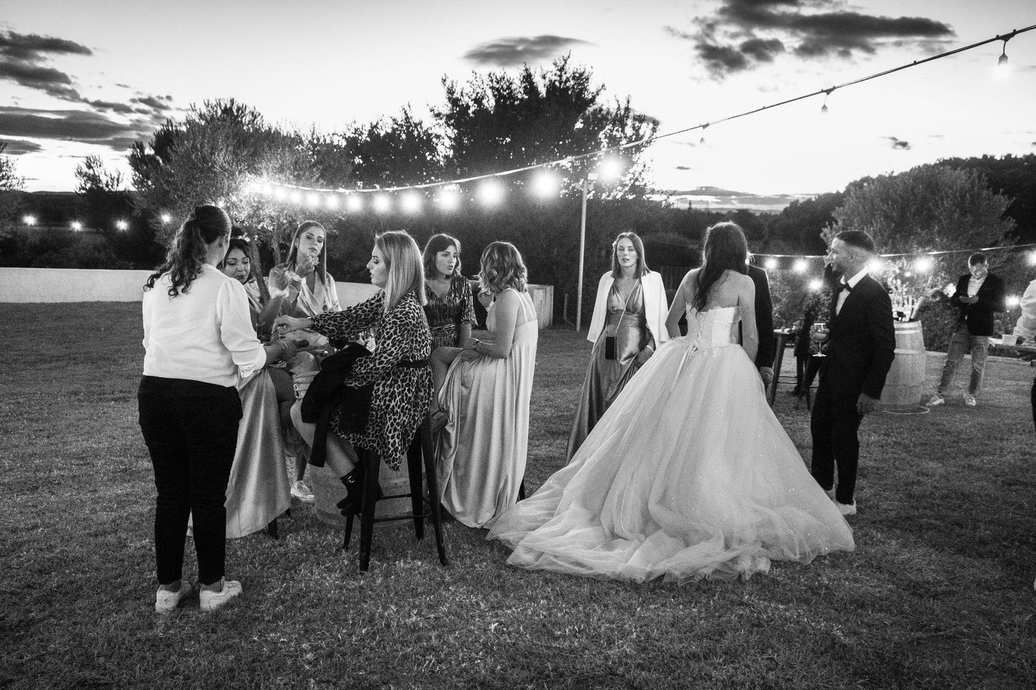 Evening wedding reception under string lights with guests mingling outdoors at sunset.