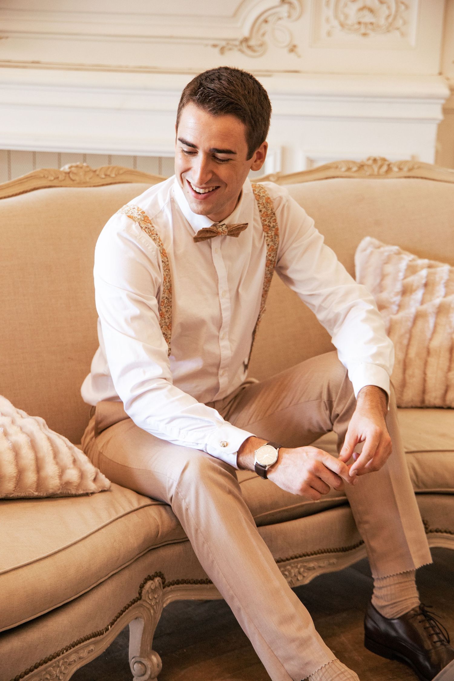 Groom in light colored suit sitting casually on elegant couch.