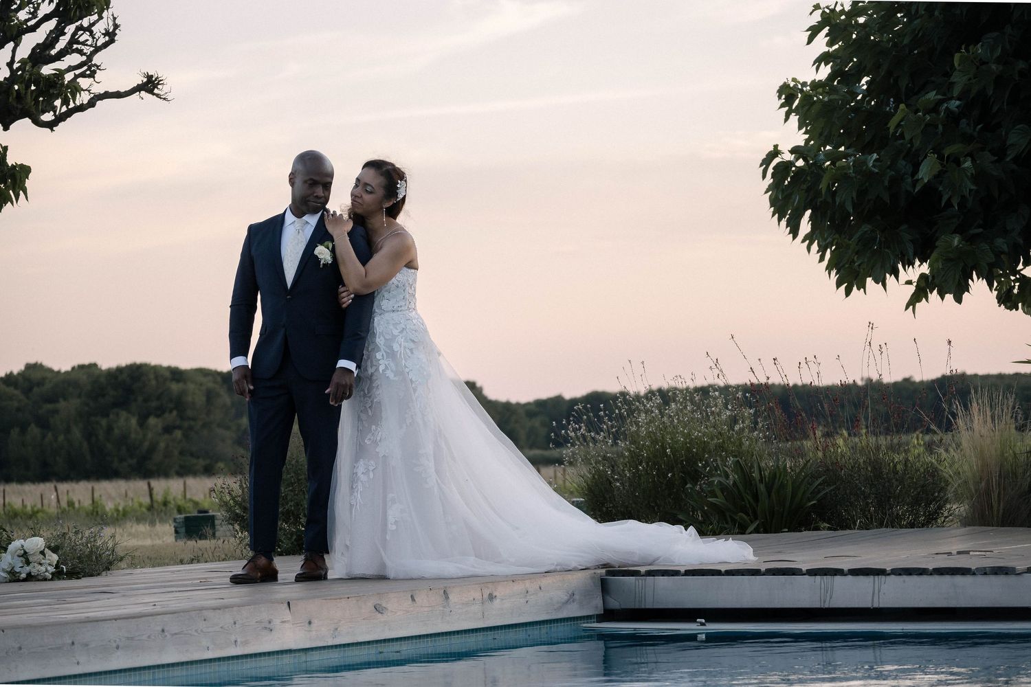 Silhouetted couple poses together against a sunset sky in their wedding attire.