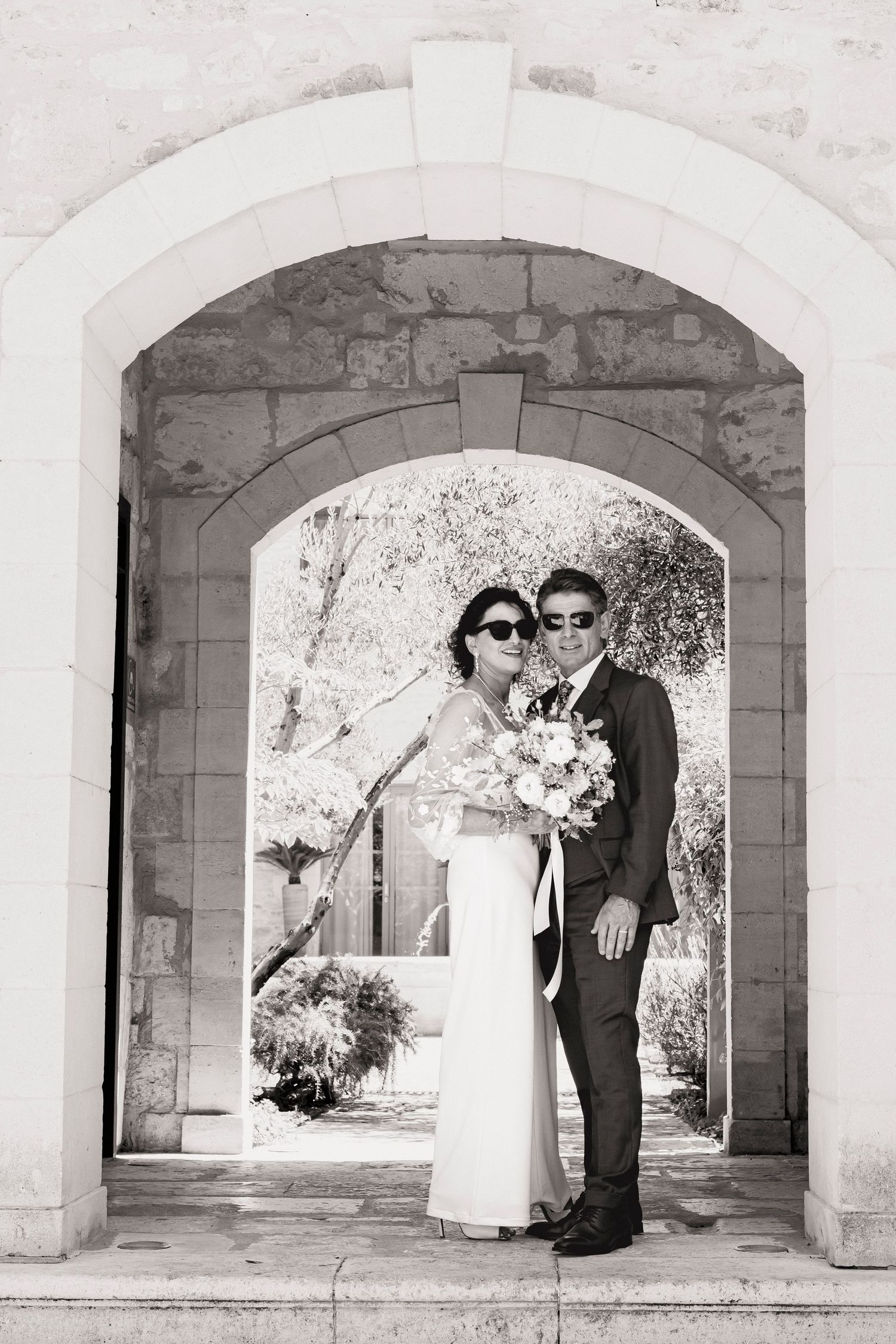 Black and white portrait of wedding couple sharing intimate moment under historic stone archway.