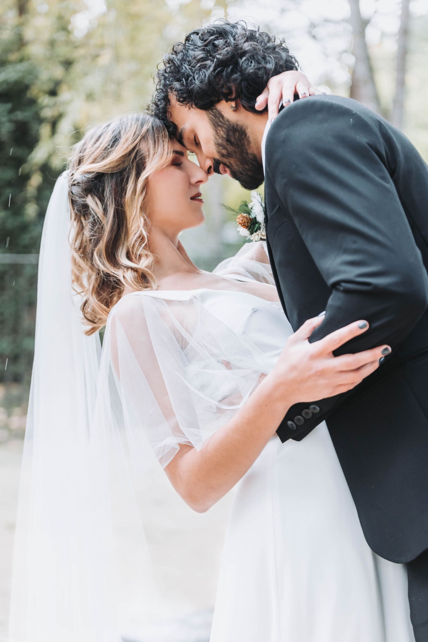 Romantic wedding couple sharing intimate kisses in an outdoor garden setting with flowing white veil and formal attire.