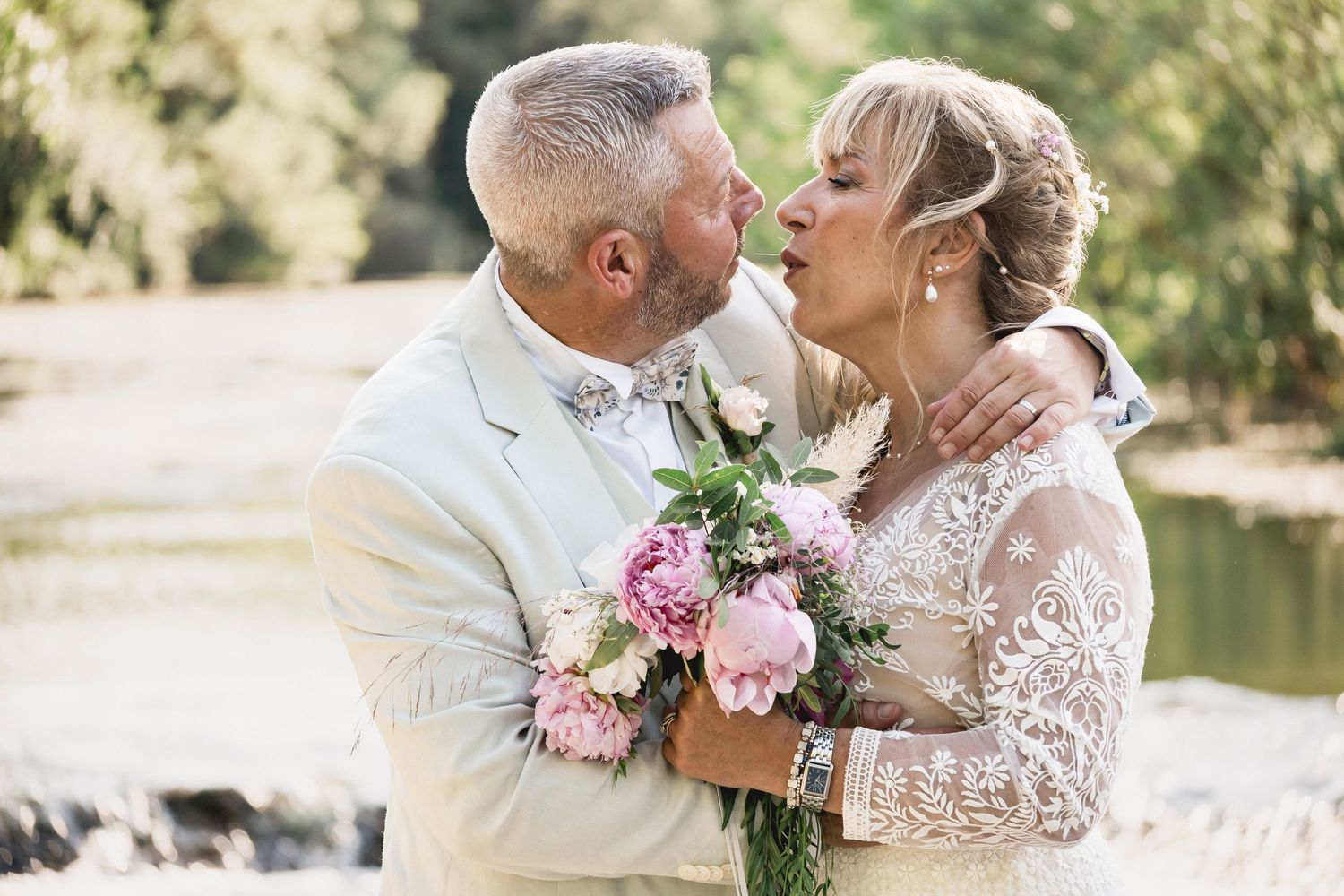 Wedding couple embraces tenderly against a sunlit garden backdrop with delicate flowers and white attire.