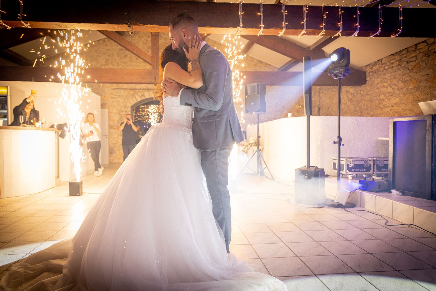 Dramatic wedding dance scene illuminated by spotlights and string lights in a rustic venue.