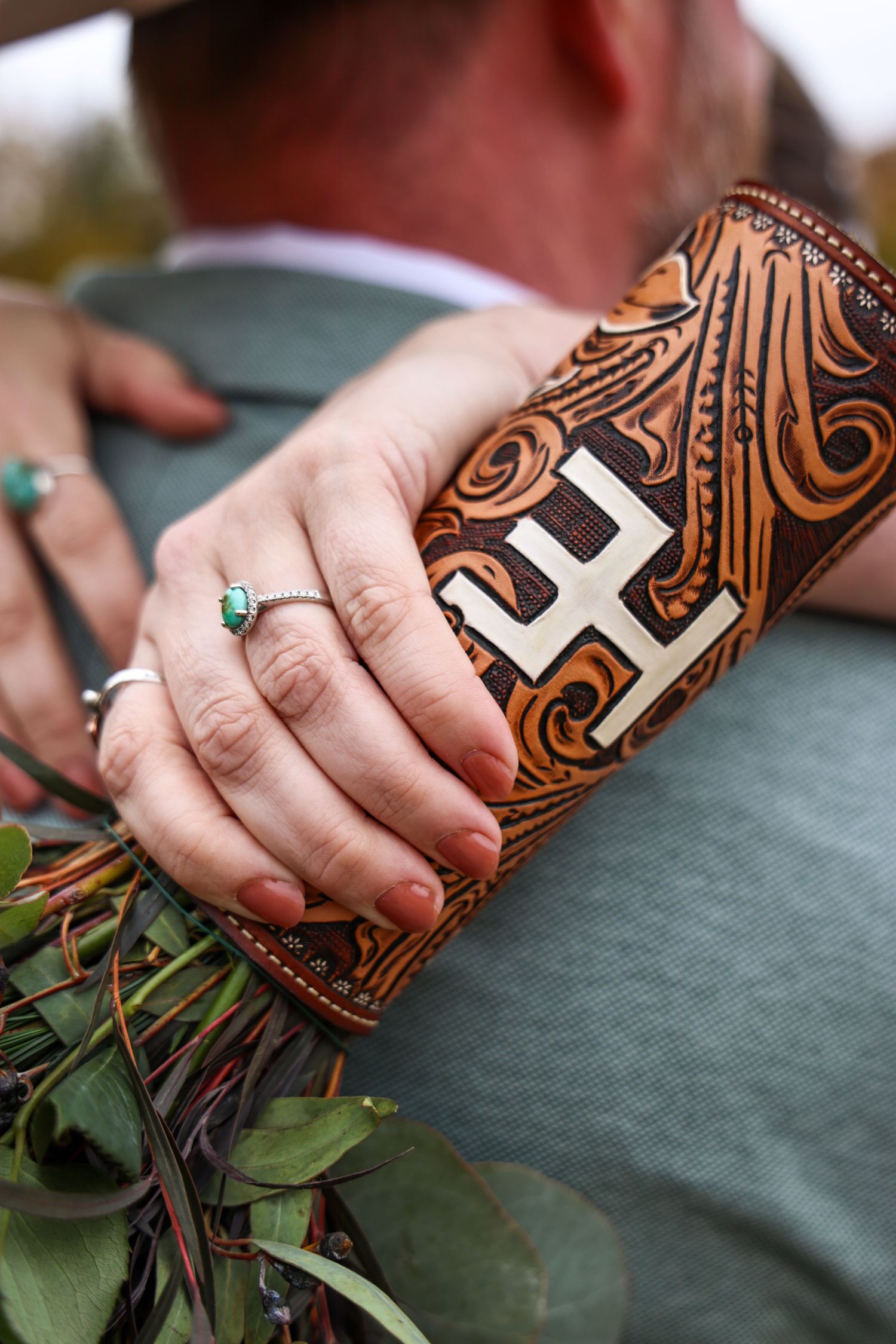 Close-up of a hand wearing a turquoise wedding ring and holding a leather wallet with decorative western tooling and letter HE brand Abilene