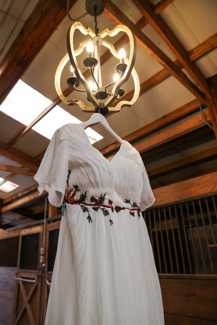 Wedding dress hanging beneath an ornate chandelier in a rustic barn setting in Abilene, Texas.
