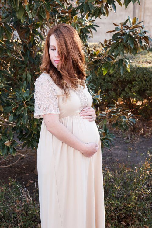 Maternity portrait of woman in white lace dress standing against magnolia tree background in Abilene, Texas.