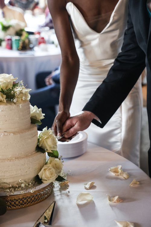 Wedding couple cutting into an elegant white tiered cake decorated with roses in Abilene, Texas.
