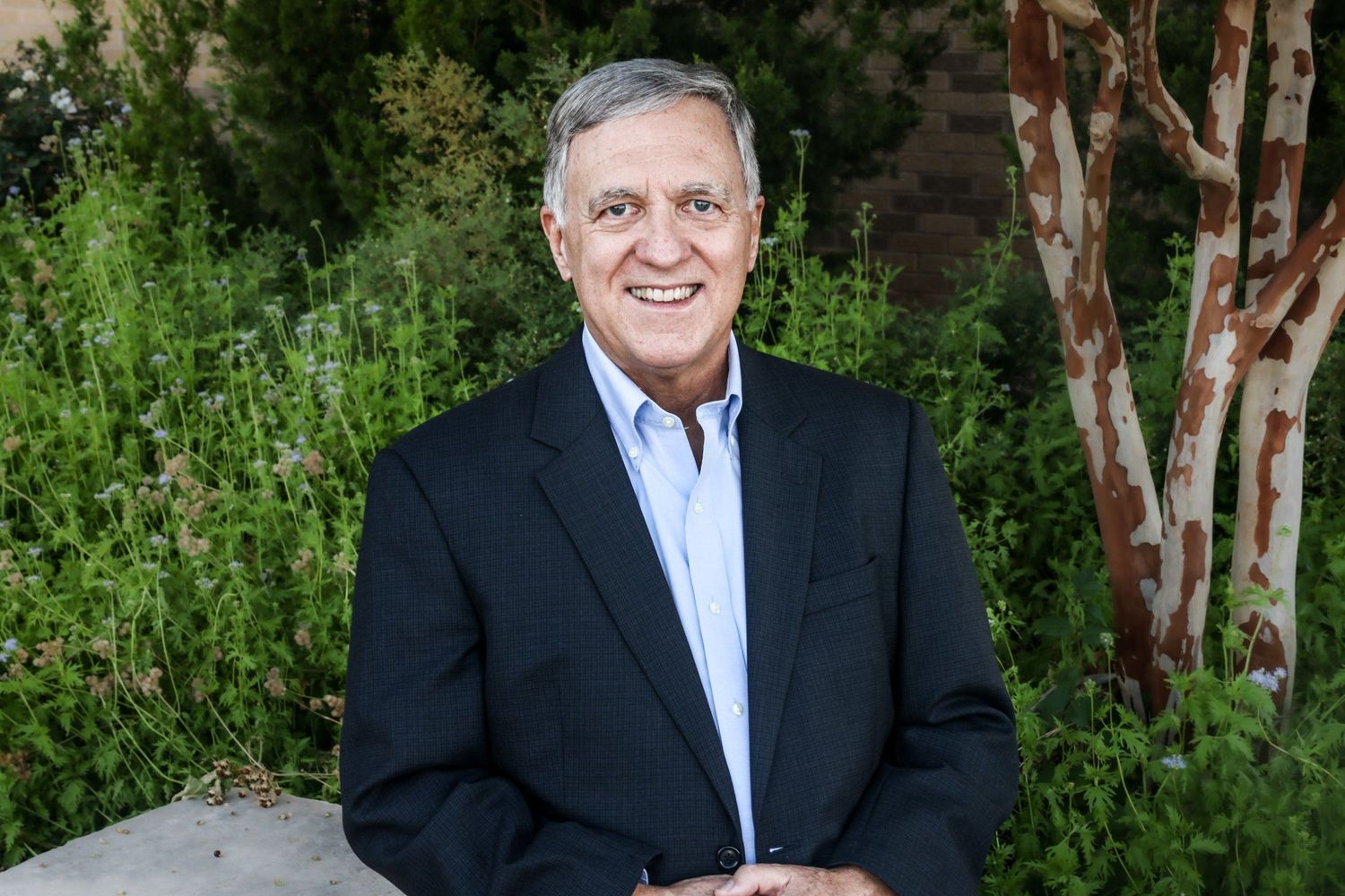 Professional headshot of businessman in navy blazer and blue shirt outdoors in Abilene, Texas.