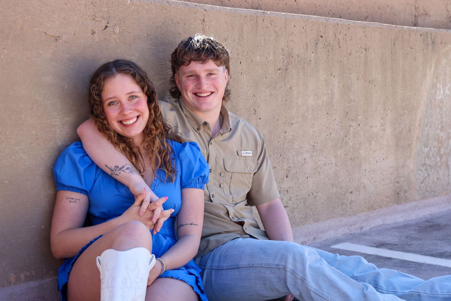 Casual couple sitting together against a concrete wall smiling and embracing outdoors  in Abilene, Texas.