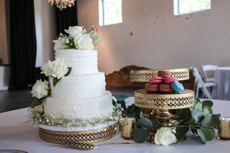 Elegant white wedding cake with floral decorations displayed on gold stands alongside colorful macarons in Abilene, Texas.