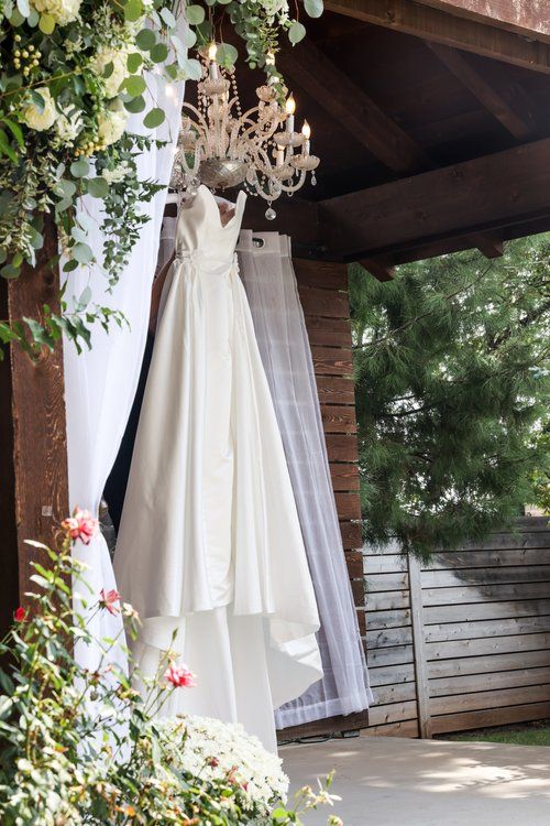 A white wedding dress hanging from a crystal chandelier with floral arrangements and greenery in Abilene, Texas.
