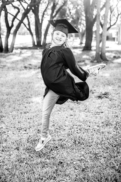 A graduate in cap and gown strikes a playful dance pose outdoors in a black and white photo in Abilene, Texas.