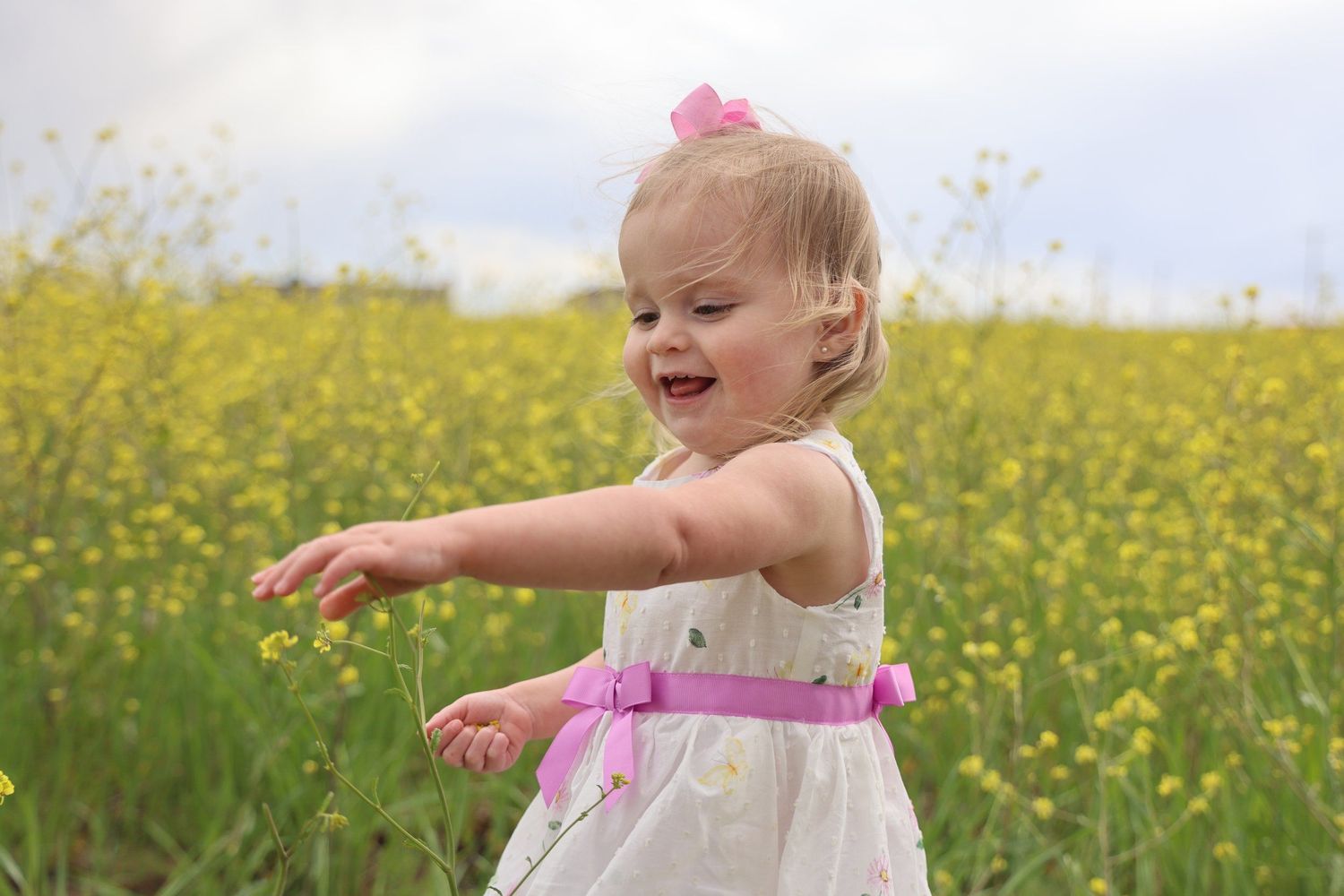 Dancing child in white dress with pink sash among blooming yellow wildflowers in Abilene, Texas.