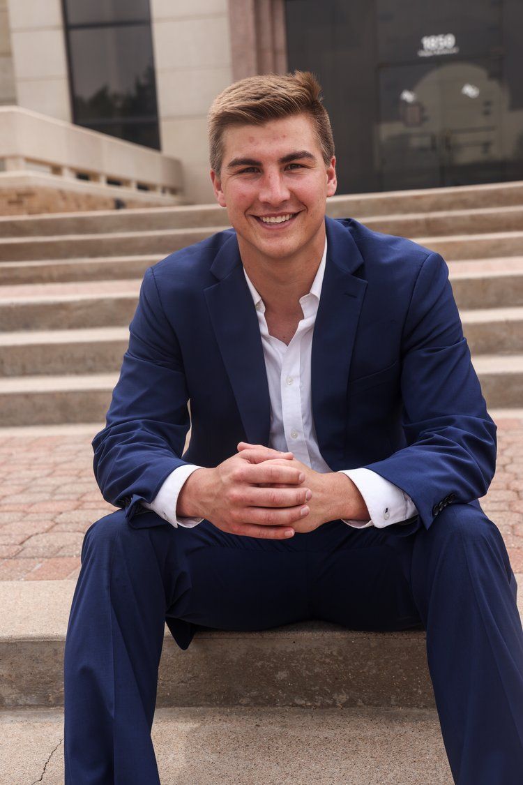 Professional headshot of person in navy suit sitting on concrete steps in Abilene, Texas.