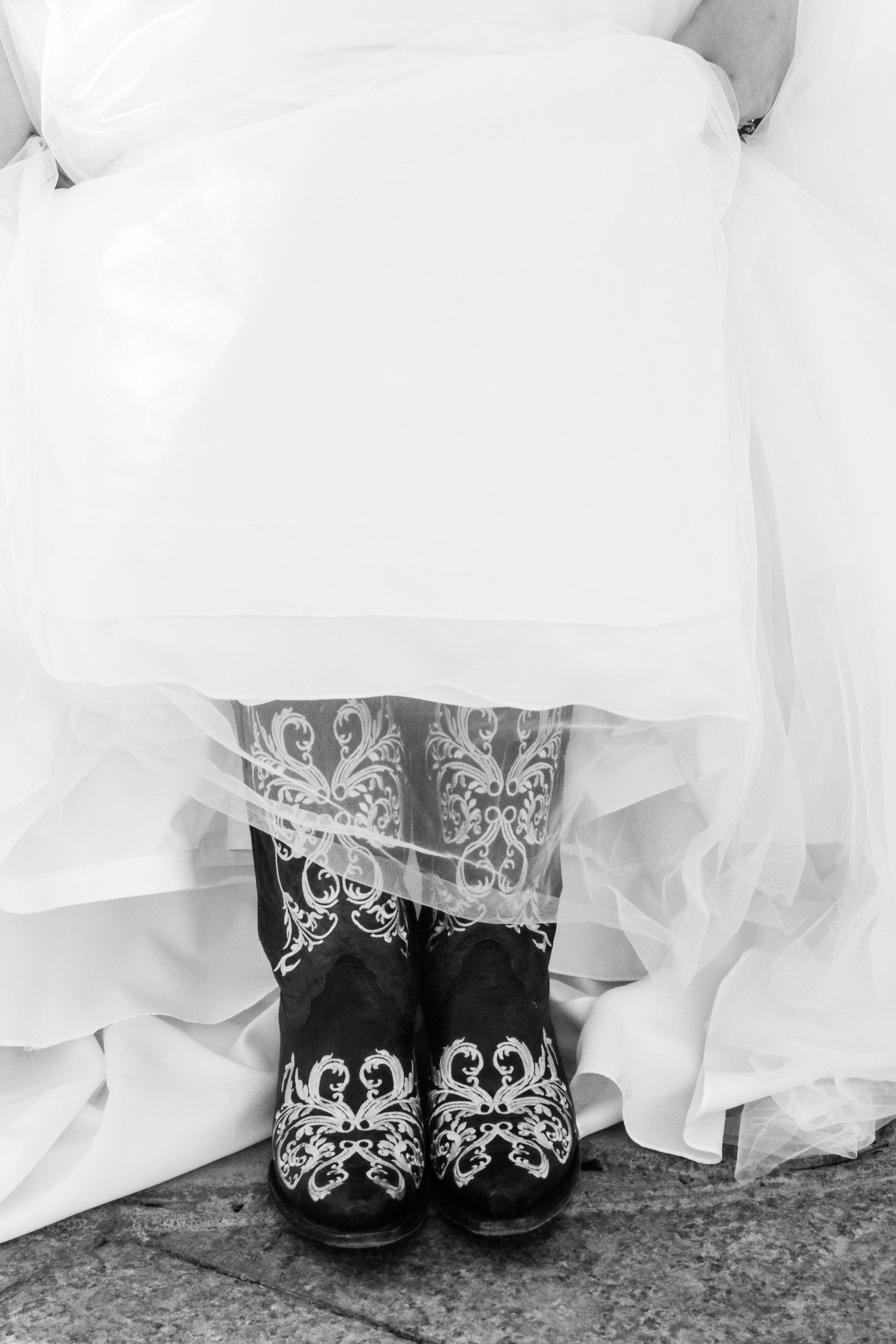 Black and white photo of embroidered cowboy boots under white wedding dress in Abilene, Texas.