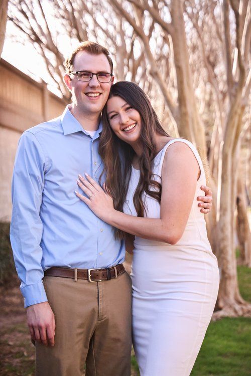 A couple embraces outdoors in front of trees wearing coordinated blue and white outfits in Abilene, Texas.