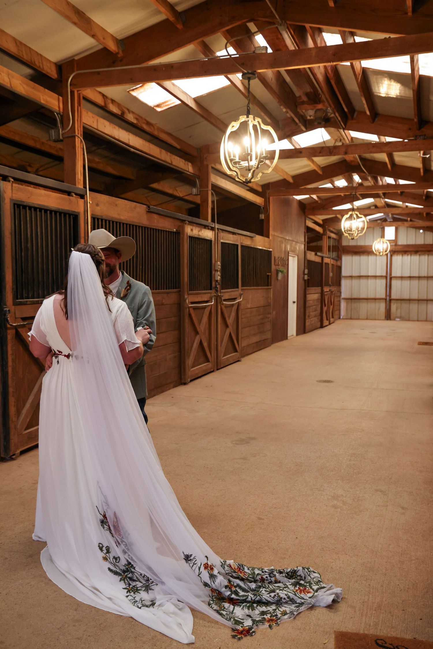 Wedding dress with floral train captured in rustic wooden horse stable interior wedding venue in Abilene Texas.