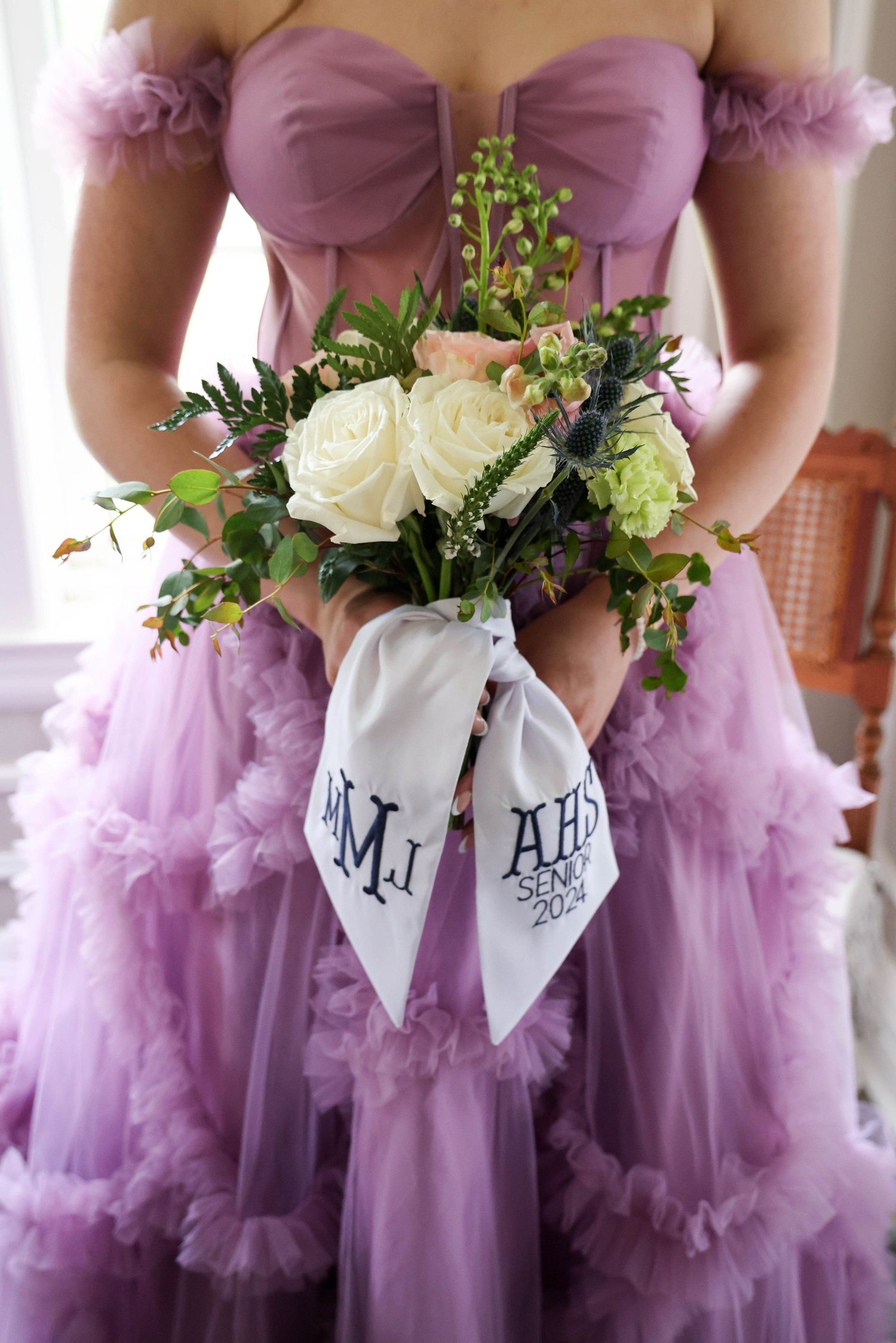 Purple tulle dress with off-shoulder design holds white rose bouquet with monogrammed ribbon in Abilene, Texas.