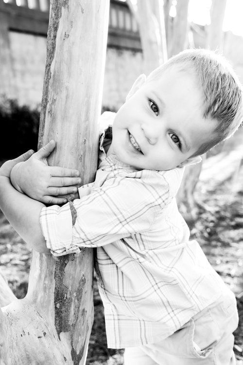 Black and white portrait of toddler playfully hugging wooden post outdoors in Abilene, Texas.