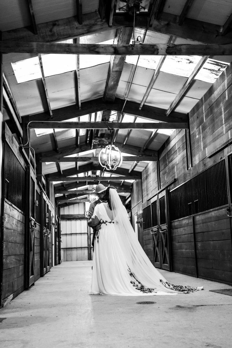 A dramatic black and white wedding photo in a rustic horse stable with a flowing white dress and veil in Abilene, Texas.