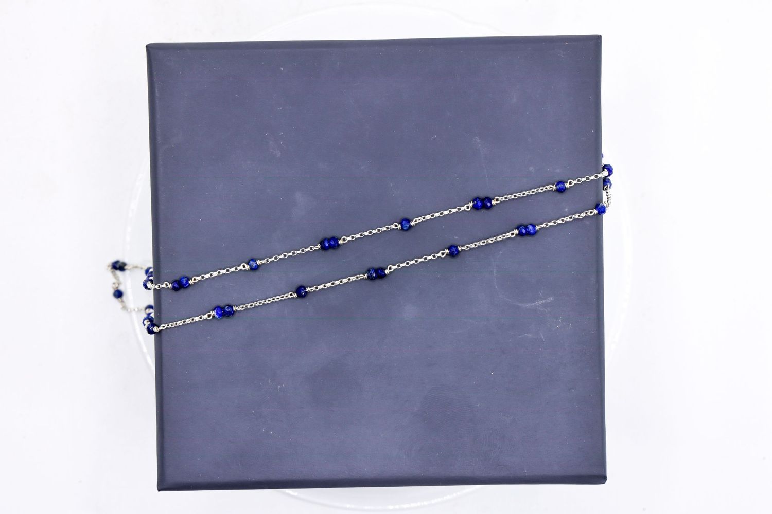 Blue sapphire and silver beaded necklace displayed on dark gray background.