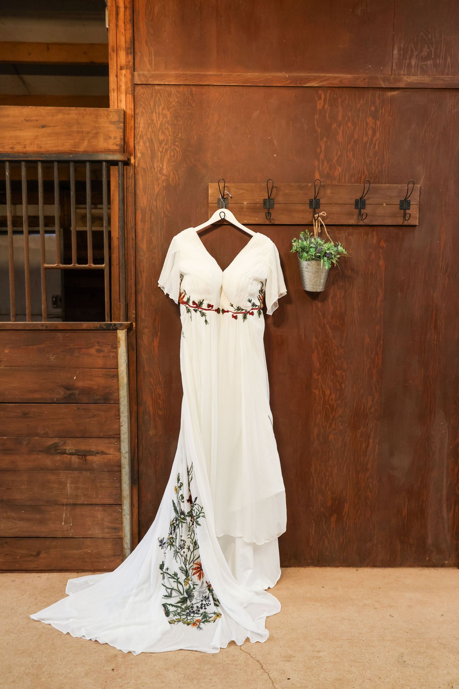 Elegant white wedding dress with floral embroidery hanging on wooden stable wall with rustic details in Abilene, Texas.
