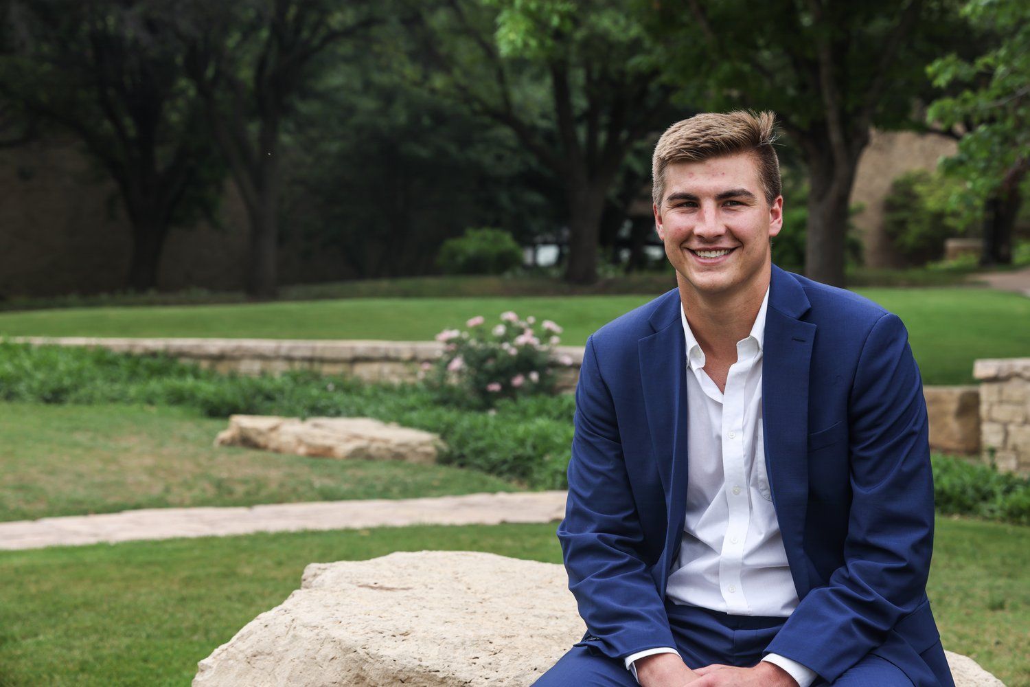 Professional headshot of young professional in navy blazer sitting outdoors in Abilene, Texas.